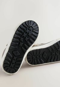 Sneakers met een gestructureerde zwarte rubberen zool met sterrenpatronen en een witte tussenzool. Lichtenbruine bovenkant van canvasmateriaal.