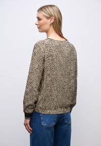 Maglietta a maniche lunghe beige con macchie leopardate nere, con scollatura rotonda, polsini elasticizzati e vestibilità rilassata. Abbinata a jeans blu.