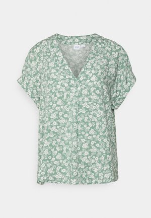Blouse verte à manches courtes en tissu doux avec un imprimé floral blanc. Présente un col en V et une coupe décontractée.
