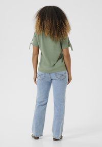 Green short-sleeve top with rolled cuffs, paired with light blue straight-leg jeans featuring decorative stitching on the back pockets.
