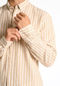 Gekraagde gestreepte blouse in lichtbeige en wit. Voorzien van knoopsluitingen, lange mouwen met manchet-details en een gestructureerde stof.