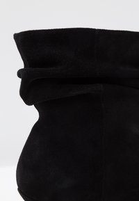 Bottine en daim noir avec un design décontracté. Présente une finition douce et texturée ainsi qu'un bord supérieur plié pour plus de détails.