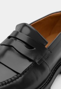 Black leather loafer featuring a smooth texture, a stitched accent across the vamp, and a contrasting brown interior lining.
