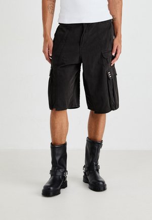 Black cargo shorts with multiple pockets, a relaxed fit, and a slightly faded texture, paired with tall black leather boots.
