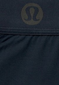 Tumesinine kangas, millel on tekstureeritud viimistlus, plektitud detailide ja keskel oleva diskreetse logoga. Sujuvad õmblused servadel.