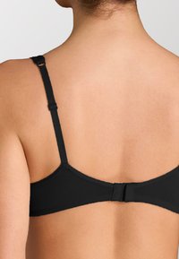 Reggiseno wireless nero con spalline regolabili, texture liscia e chiusura a gancio e occhio sul retro. Design semplice senza decorazioni.