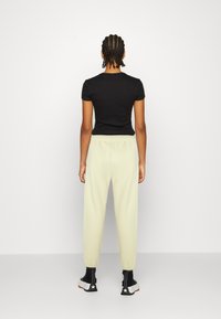 Černý top s krátkým rukávem v kombinaci se světle žlutými kalhotami na gumu. Kalhoty mají zúžený střih a doplňují je černé kotníkové boty.