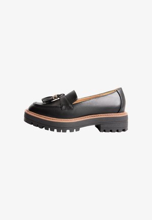 Mocassino in pelle nera con suola spessa scolpita, bordo intersuola color cuoio e nappine decorative sulla parte superiore, mostrato di profilo laterale.