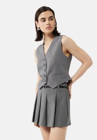 Gilet gris avec un col en V et six boutons, associé à une jupe plissée assortie et une ceinture noire. Texture lisse, design ajusté.