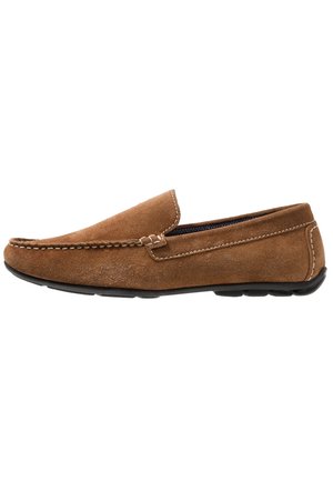 Mocassin homme en daim marron avec semelle en caoutchouc noire et coutures blanches visibles le long des bords et du dessus.