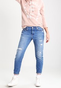 Světlé modré džíny s opotřebením, mají rovný střih a ohrnuté kotníky. Doplněné růžovou mikinou a bílými teniskami.