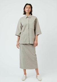 Chemise surdimensionnée à col boutonnière en coton gris clair avec des manches courtes et une poche poitrine ; associée à une jupe longue assortie.