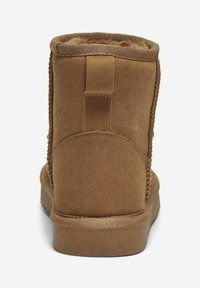 Botín de ante marrón con un interior suave, que presenta una costura trasera texturizada y una suela plana y duradera. Diseño minimalista, sin adornos.