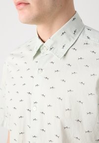 Cămașă scurtă cu mânecă, de culoare verde deschis, cu guler cu butoni, având un model repetat de pești negri și un material texturat.
