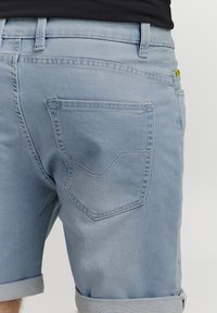 Ljust blå denimshorts med uppvikta fållar, med en bakficka med en distinkt vinklad design och synliga sömnadsdetaljer.