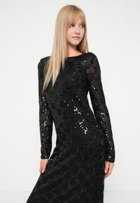 Vestido preto de manga longa, com lantejoulas por todo o tecido, silhueta justa e decote arredondado com um padrão texturizado.