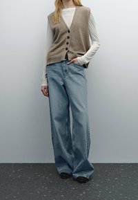 Vaaleanbeige neuleliivi mustilla napeilla, kerroksittain valkoisen pitkähihaisen paidan päällä. Yhdistettyinä löysiin vaaleansinisiin farkkuihin ja mustiin kenkiin.