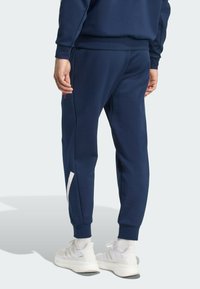 Navy blue joggers with a slim fit, made of soft fabric, featuring a white side stripe and elastic cuffs. Paired with white athletic shoes.