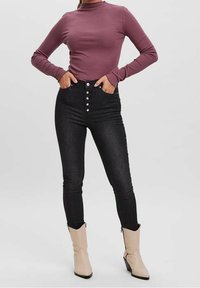 Lila gerippter Langarmoberteil, kombiniert mit hochgeschnittenen schwarzen Skinny Jeans mit silbernem Knopfverschluss, getragen mit beigen Ankle Boots.