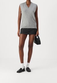 Šedý bezrukávový pletený svetr s výstřihem do V, doplněný černou mini sukní. Černé mokasíny a bílé ponožky, držící malou černou kabelku.