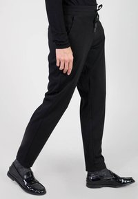 Svarta tapered-byxor med dragsko i midjan, sidofickor, slät tygkvalitet och slim fit, kombinerat med glänsande svarta loafers och grå strumpor.