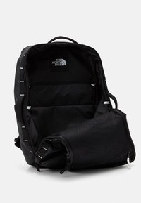Sac à dos noir North Face ouvert pour montrer le compartiment principal et la poche zippée en mesh sur un fond clair uni.