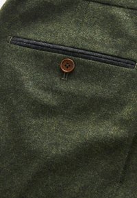 Tissu en laine vert avec une apparence texturée, comportant un unique bouton marron et un détail de poche zippée gris foncé.