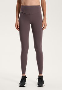 Legginsy o wysokim stanie w stonowanym kolorze mauve, wykonane z gładkiego, elastycznego materiału. Posiadają bezszwowy przód i dopasowany krój.