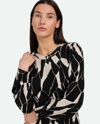 Zwarte en beige gemusterde blouse met lange mouwen, ronde halslijn, knoopsluiting en een textuurstof met abstracte vormen.