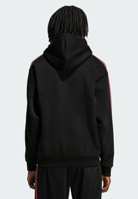 Čierna mikina s kapucňou a červenými bočnými pruhmi, s voľným strihom, rebrovanými manžetami a lemom. Hladká textúra a neformálny dizajn.
