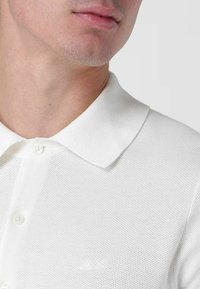 Polo bianco caratterizzato da un tessuto a rete testurizzato, colletto classico e chiusura con bottoni, con un logo ricamato in modo discreto sul petto.