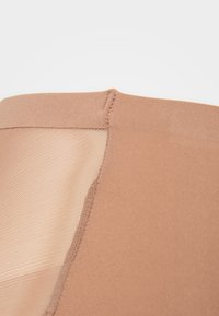 Bra top in light tan fabric featuring a mesh inset, seamless edge, and smooth texture. Stitch detailing along the seams.