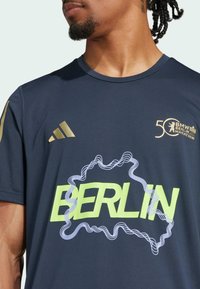 Navy blue athletic shirt featuring a large yellow "BERLIN" graphic, gold accents, and the BMW Berlin Marathon logo on the chest.
