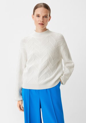 White knit sweater featuring a textured chevron pattern and a high neckline, paired with bright blue wide-leg trousers.