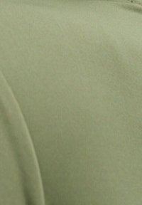 Olivgrönt tyg med en mjuk struktur och lätt glans. Materialet verkar stretchigt med en vikt kant till höger.