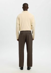 Beżowa koszula polo z długim rękawem w luźnym fasonie, sparowana z brązowymi spodniami garniturowymi o gładkiej fakturze i dwóch tylnych kieszeniach.