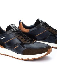 Zapatillas deportivas con una combinación de cuero azul marino y ante marrón oscuro, con una entresuela blanca y una suela de goma marrón. Detalles en color naranja.