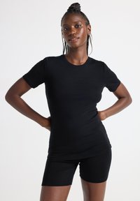 Svart ribbad topp med kort ärm i kombination med svarta tajta shorts. Tyget verkar mjukt med en slät yta och en klassisk rund halsringning.