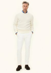 Sweter w warkocz, jasnoniebieska koszula z kołnierzykiem, białe spodnie i ciemnobrązowe zamszowe buty. Strukturalny design z teksturowanymi detalami.