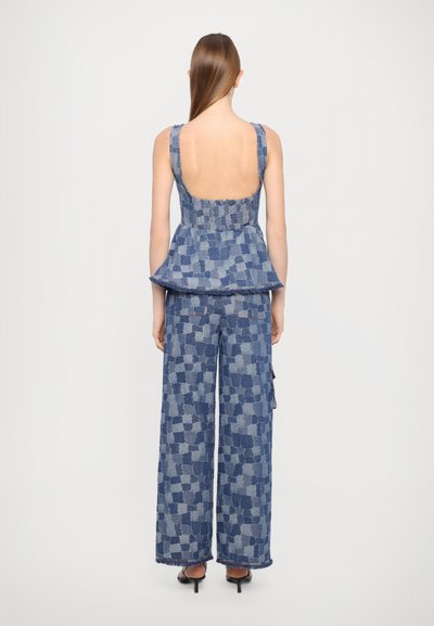 Denim peplum top s otvoreným chrbtom, skombinovaný s nohavicami s širokými nohavicami s károvaným vzorom v rôznych odtieňoch modrej.
