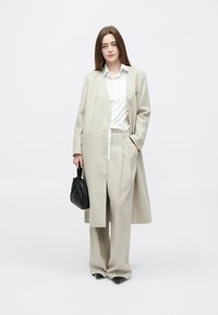 Jasnoszary garnitur z mieszanki wełny z dopasowanym długim płaszczem i szerokimi spodniami, zestawiony z białą koszulą i małą czarną torebką.