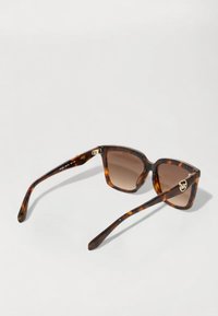 Ochelari de soare din material tortoise cu lentile pătrate, nuanță de gradient maro, accente aurii pe tâmplă și finisaj elegant, lustruit.