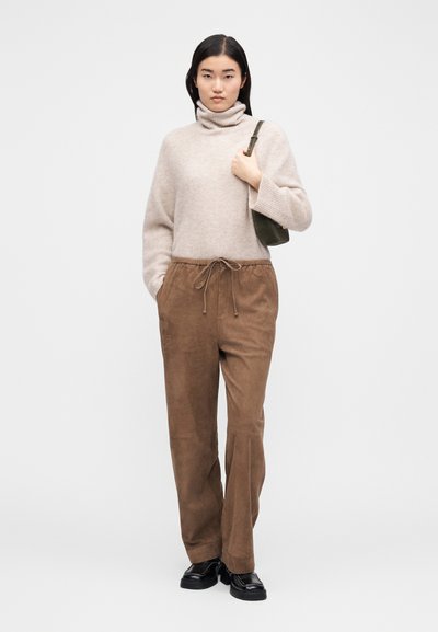 Lazackrém színű garbóvédu felső, laza szabású. Barna, húzózsinóros nadrág, sima textúrával. Fekete cipők. Egyszerű zöld válltáska.