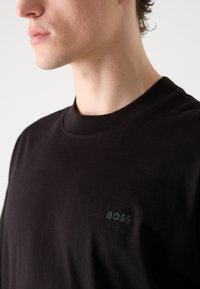 Juodas medvilninis marškinėliai su apvalia iškirpte, puošti subtiliu BOSS logotipu toje pačioje juodoje spalvoje, esančiu ant krūtinės. Lygus paviršius ir prigludusi forma.