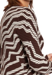 Brun och vit mönstrad stickad tröja med zigzag-randiga mönster och texturert tyg. Närbild på ärmen och axeln.