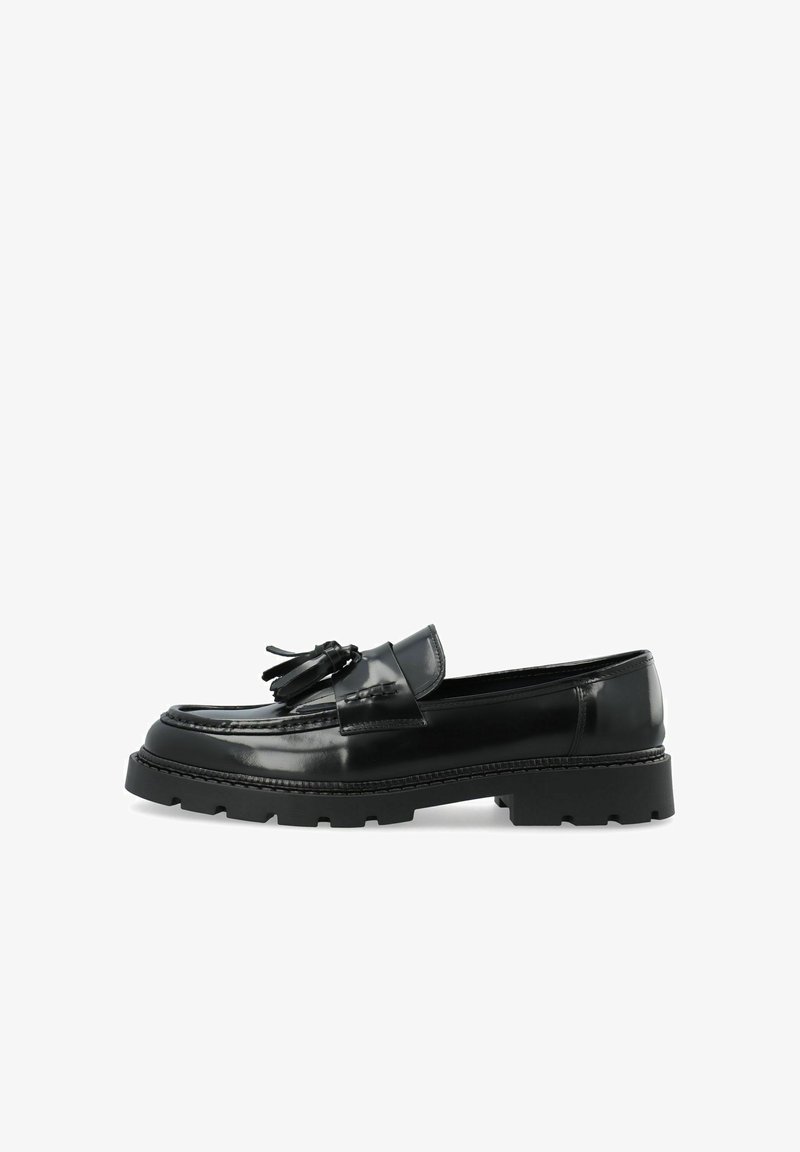Mocassin en cuir noir brillant avec pompons et semelle épaisse et volumineuse, présenté de profil sur fond blanc.