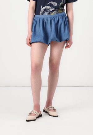 Blaue Leinen-Shorts mit elastischem Bund, locker geschnitten und mit leichter Textur. Kombiniert mit beigen, spitzen Slip-On-Schuhen.