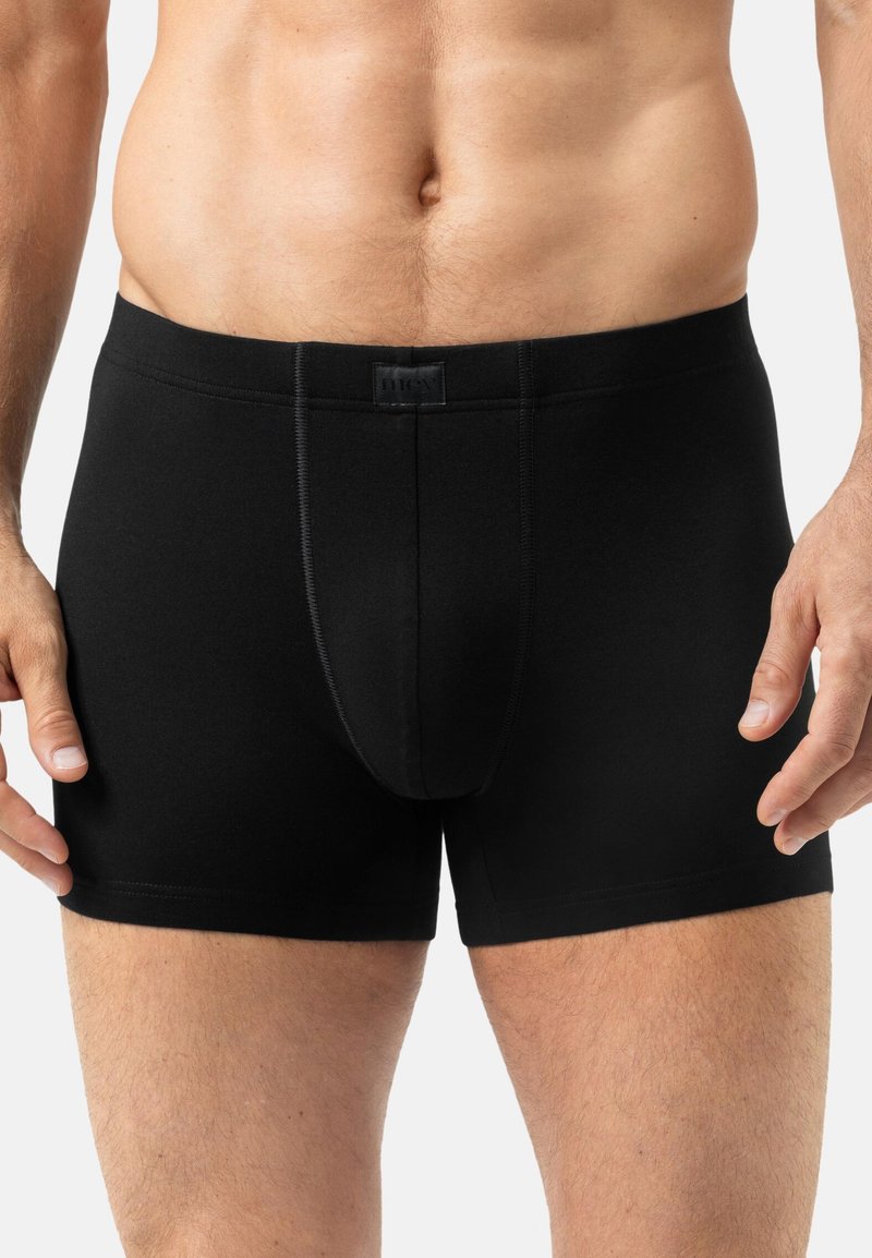 Uomo che indossa semplici boxer neri, in piedi con le braccia rilassate lungo i fianchi, che mostra il torace e la parte superiore delle cosce.