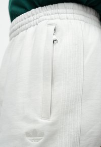 Calças de jogging de fleece branco com superfície texturizada, cintura elástica, bolso lateral com fecho éclair e detalhe de logótipo bordado na perna.