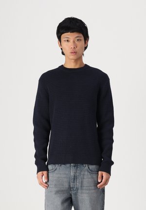 Pulover tricotat bleu închis cu un model texturat, guler rotund și mâneci lungi, asortat cu blugi din denim de un albastru deschis.